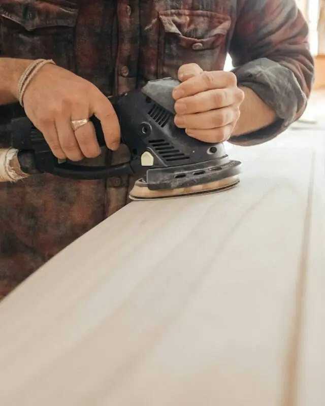Hands sanding a wood board with an orbital sander