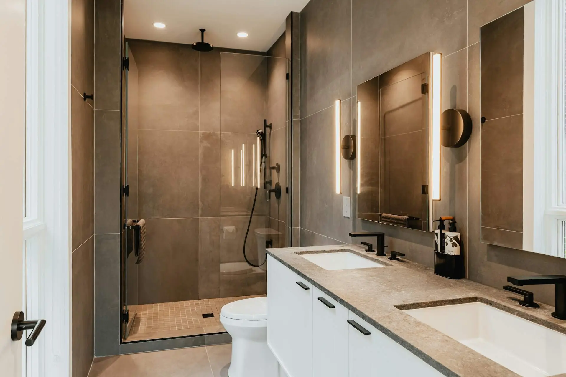 Bathroom with a large-format stone tile shower, black fixtures and a double vanity with warm wall lights