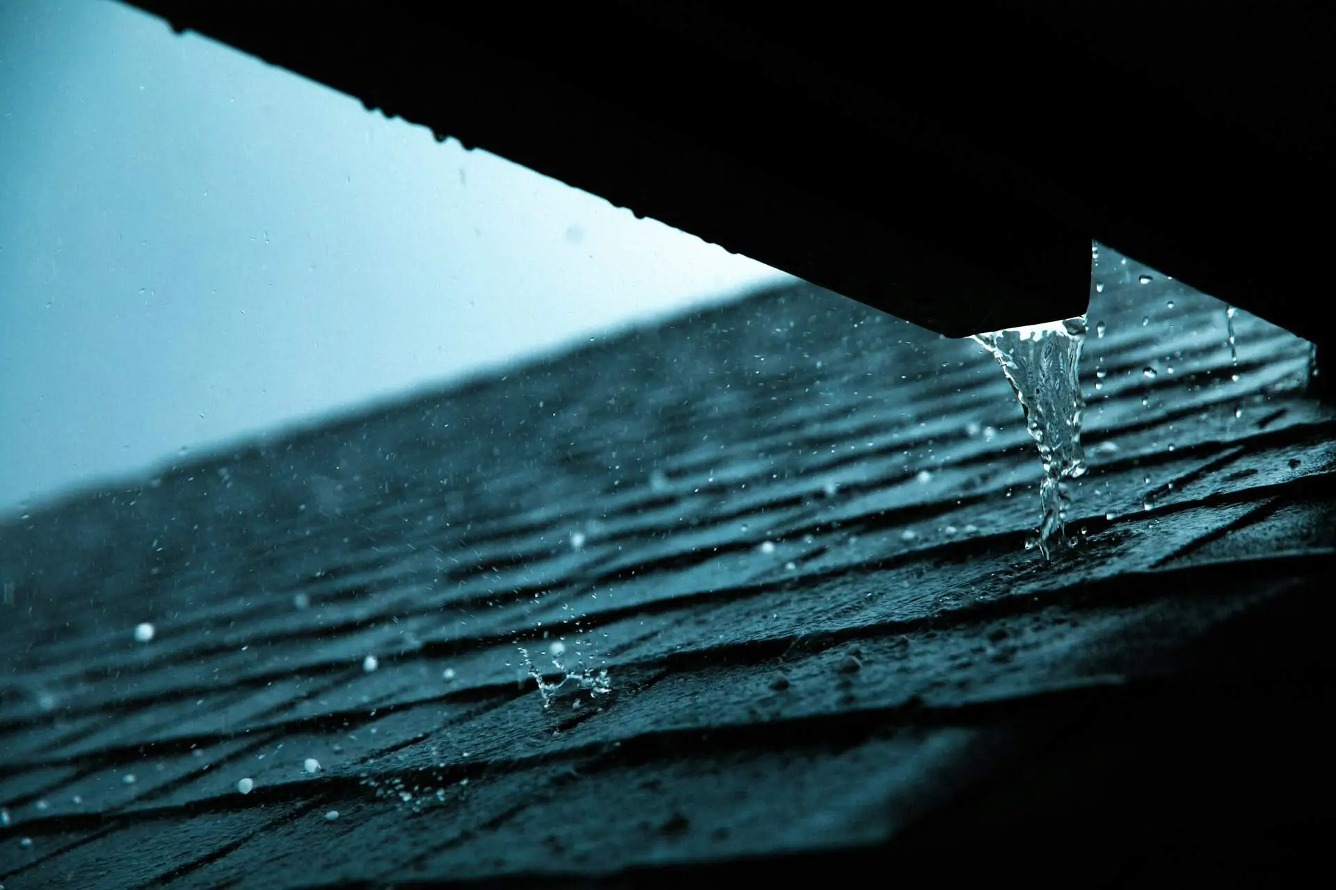 Rain running off a gutter onto dark asphalt shingles