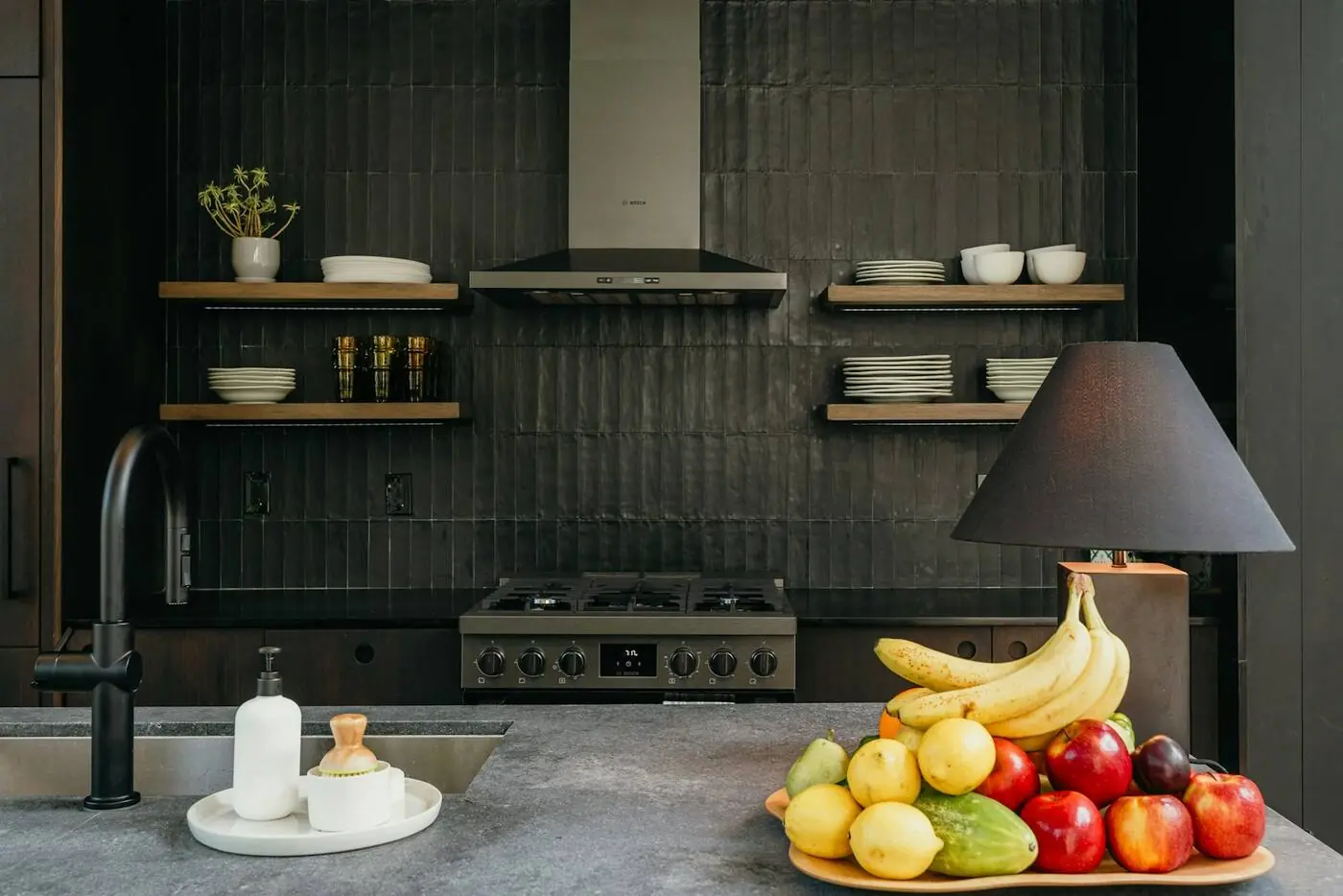 A finished kitchen: dark tile wall, oak shelves, a range and hood, and a stone island